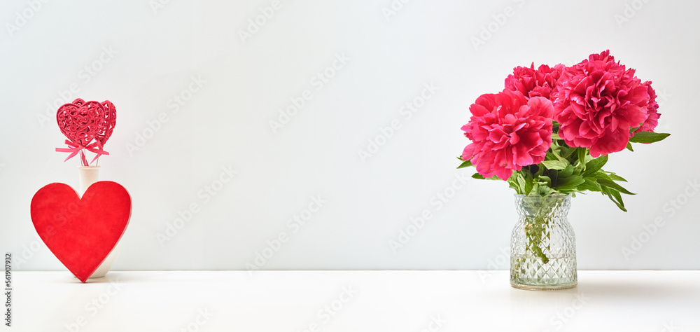 Red peonies in a vase and red heart on a white table with copy space. Mock up for displaying works. Valentine's day holiday background concept Red peonies in a vase and red heart on a white table with copy space. Mock up for displaying works. Valentine's day holiday background concept