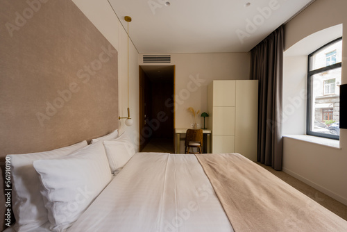 comfortable bed with white bedding near desk and chair in modern hotel bedroom. © LIGHTFIELD STUDIOS