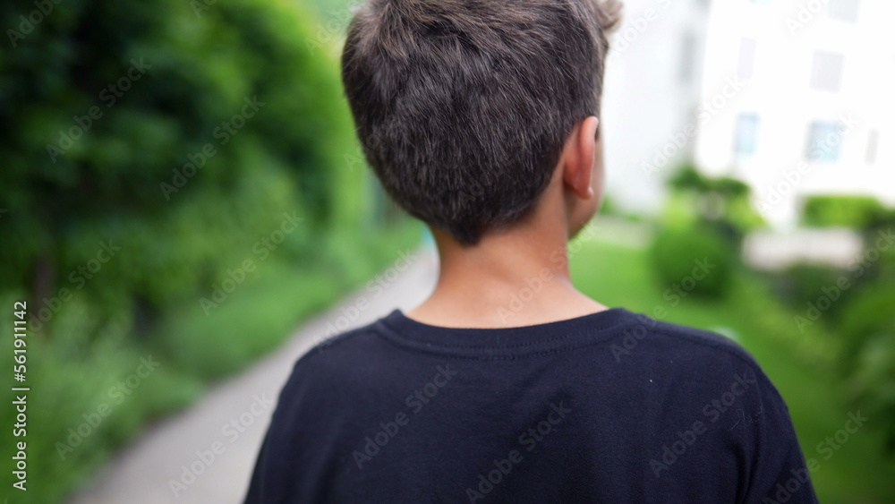 Back of young boy walking outside at park. Pensive child daydreaming Back of young boy walking outside at park. Pensive child daydreaming