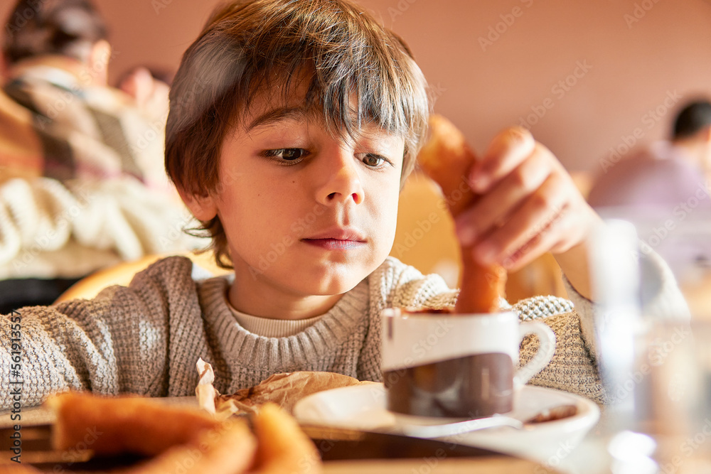 elementary age kid dipping churros into a hot chocolate mug elementary age kid dipping churros into a hot chocolate mug