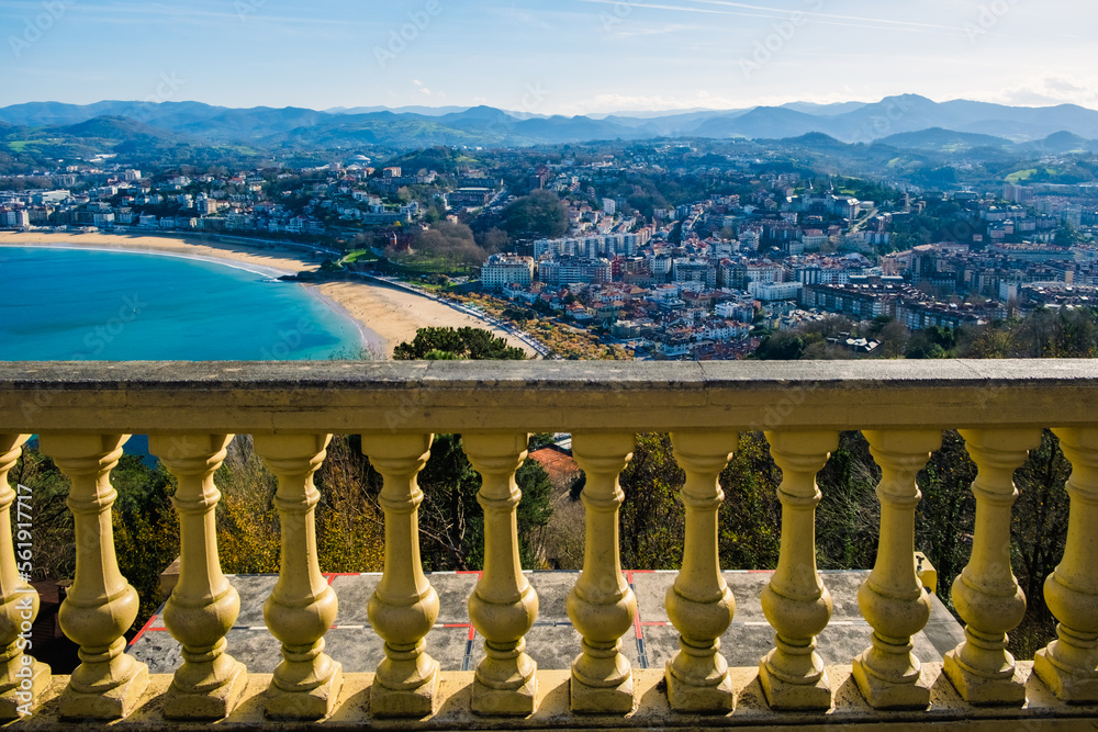 An old railing separates a cliff, with the city of San Sebastian and the sea in the background.