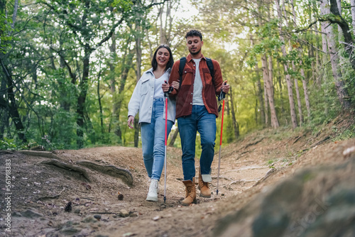 A couple is hiking and chatting about interesting topics, surrounded by breathtaking nature and greenery. Trekking poles are helping them with the bumpy trail.