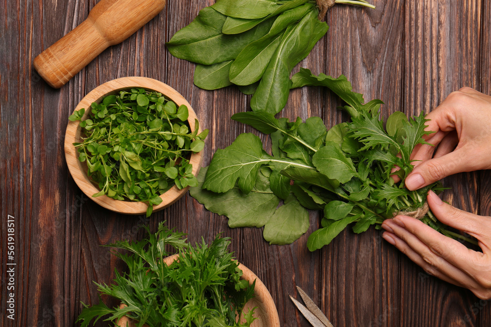 Woman with fresh green herbs at wooden table, top view