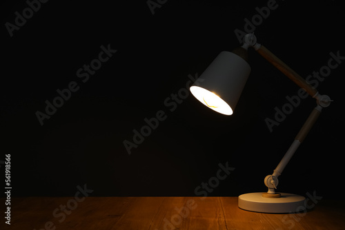 Stylish modern desk lamp on wooden table at night, space for text