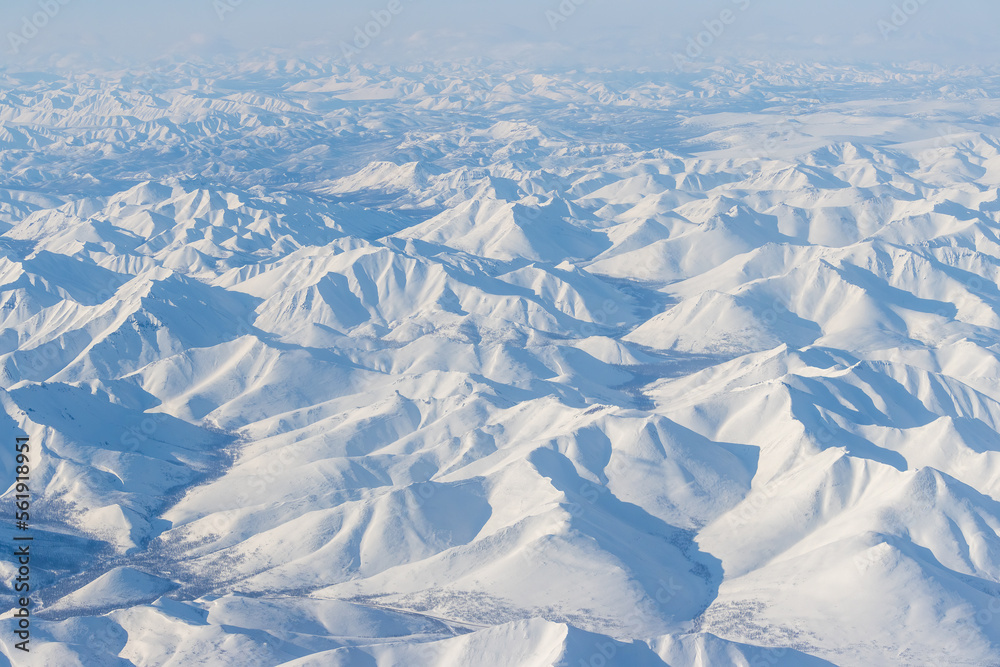 Obraz premium Aerial view of snow-capped mountains. Winter snowy mountain landscape. Air travel to the far North of Russia. Kolyma Mountains, Magadan Region, Siberia, Russian Far East. Great for the background.