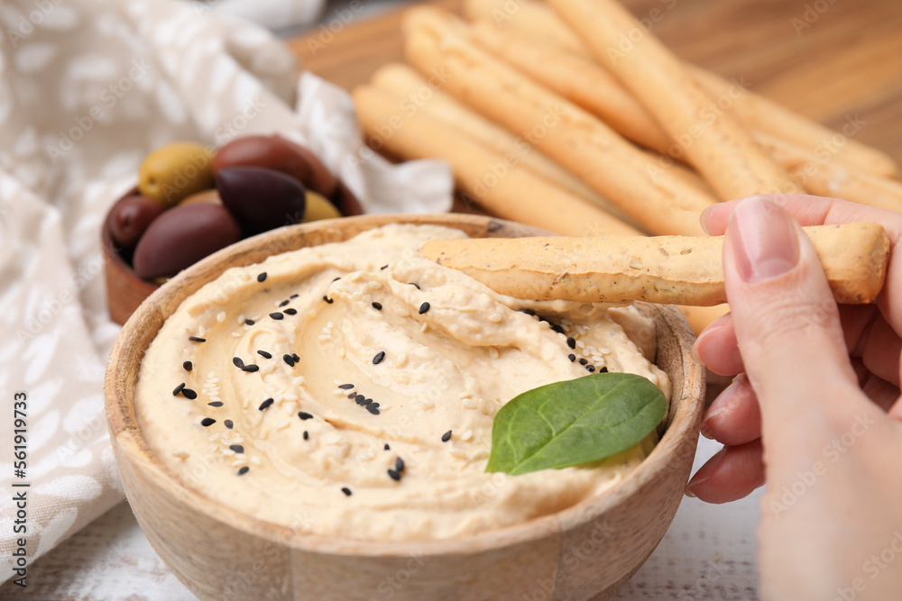 Fototapeta premium Woman dipping tasty grissini stick into hummus at white wooden table, closeup