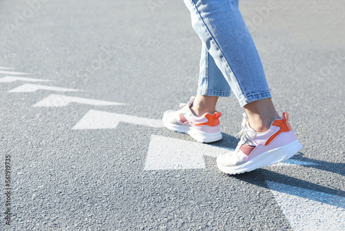 Planning future. Woman walking on drawn marks on road, closeup. White arrows showing direction of way photo