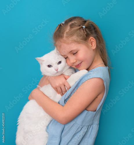 Little girl hugging her pet white cat over blue background.