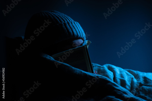 woman wears a beanie and reading in her room and hiding her face with book in a blanket close portrait   blue lights   © Gleb Minich