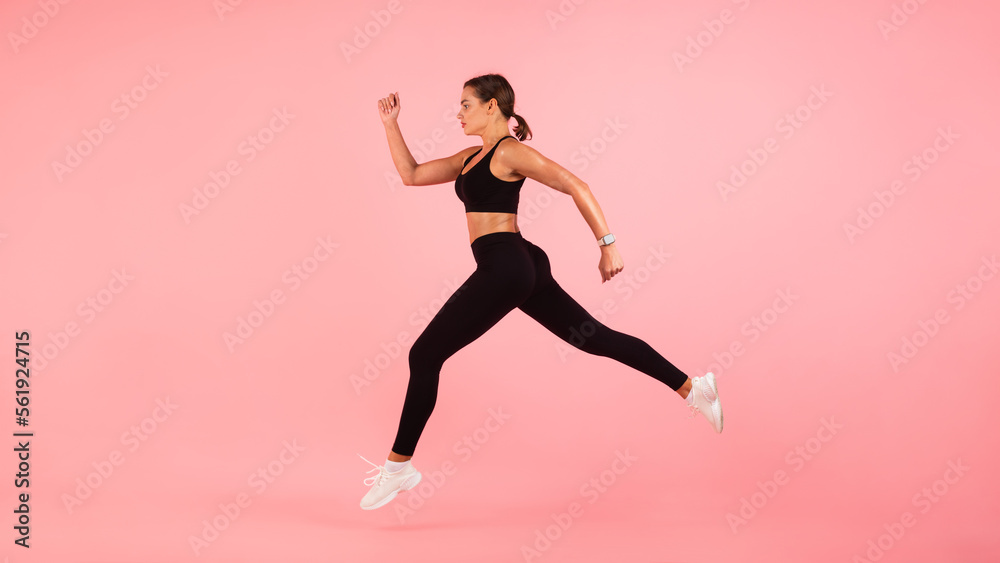 Motivated Sporty Young Woman Running In Mid-Air Over Pink Background
