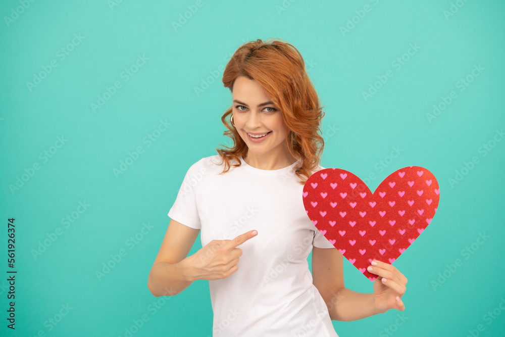happy young woman with red heart on blue background. point finger happy young woman with red heart on blue background. point finger