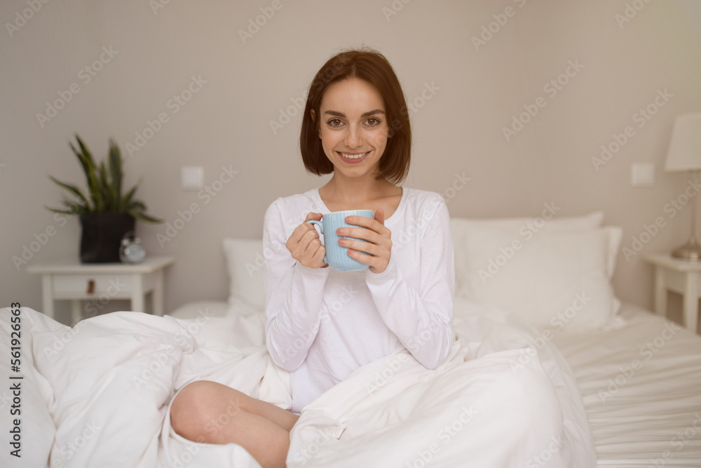 Candid photo of cheerful young woman drinking coffee in bed Candid photo of cheerful young woman drinking coffee in bed