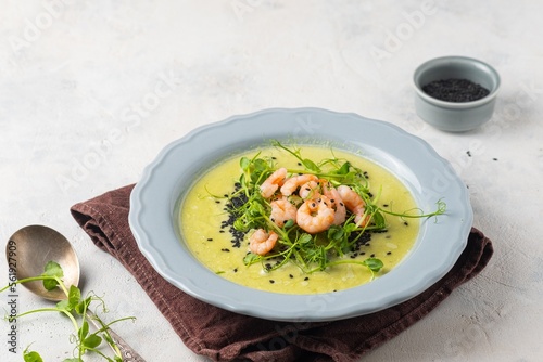 Green pea soup with pea microgreens, black sesame and shrimp in a gray plate on a light concrete background. Soup recipes.