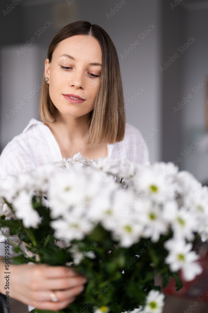 Happy and joyful young woman in white arranging white flowers at home in the kitchen Happy and joyful young woman in white arranging white flowers at home in the kitchen
