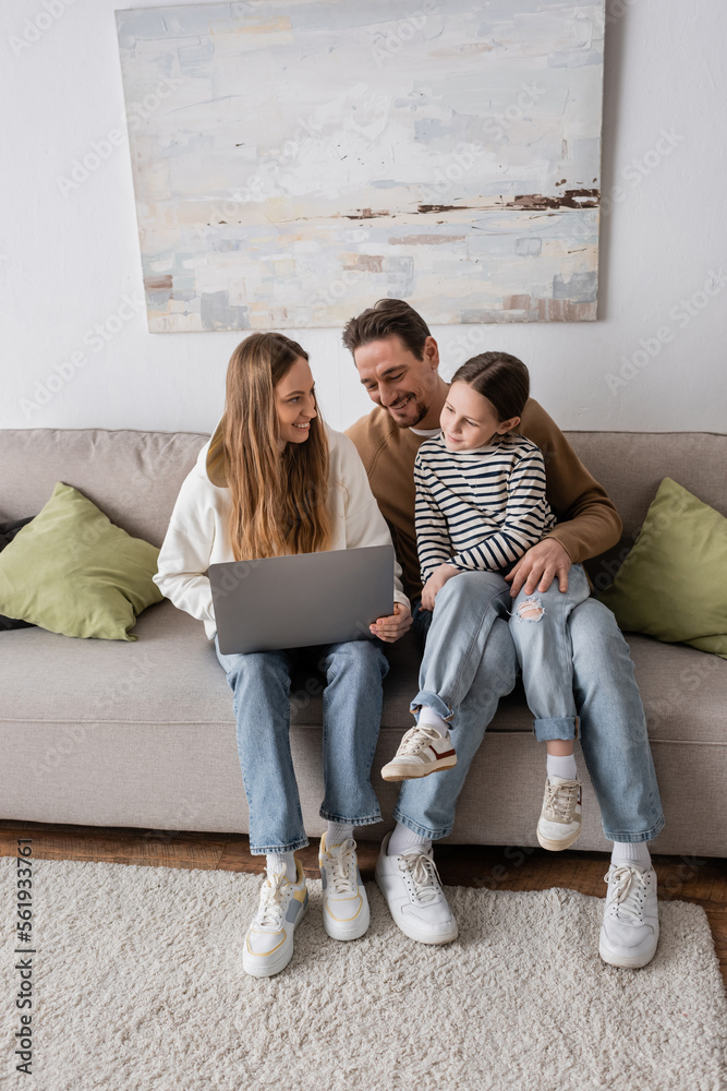 full length of happy woman sitting with laptop near husband and daughter in living room. full length of happy woman sitting with laptop near husband and daughter in living room.