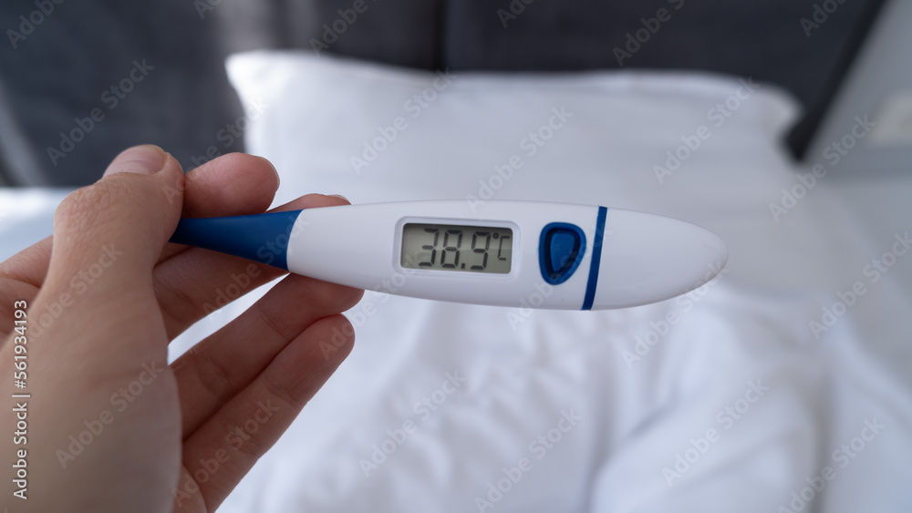 Obraz premium Checking temperature at home in bed with digital thermometer, high body temperature, fever, self monitoring, Health and Medical concept