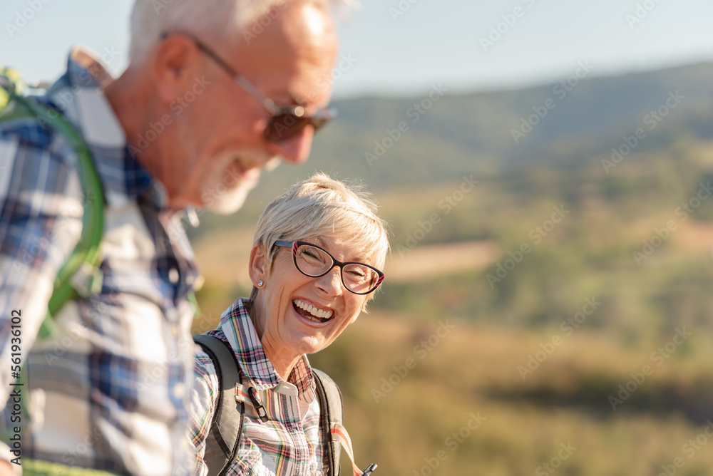 Portrait of an cheerful active senior Caucasian couple hiking in the mountains with backpacks and hiking poles, enjoying their adventure