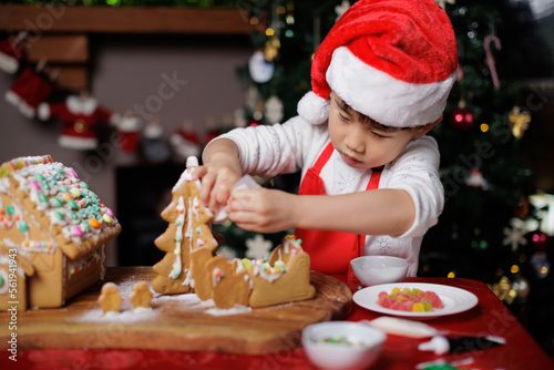 young girl wearing Santa hat was decorating gingerbread house for celebrating Christmas at home