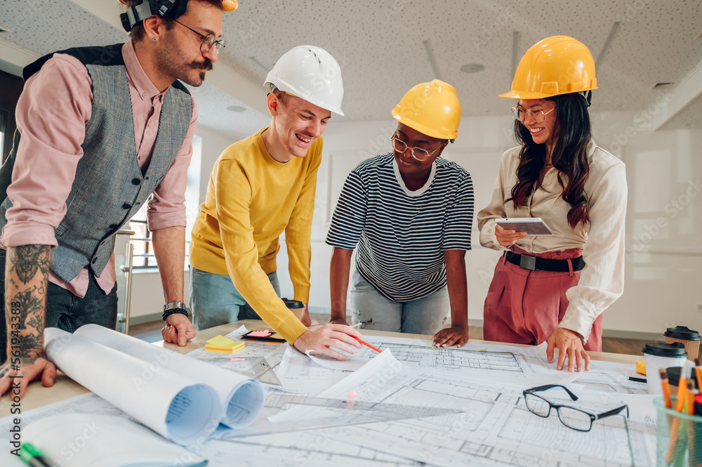 Multiracial team of architects having a meeting while using blueprints Multiracial team of architects having a meeting while using blueprints