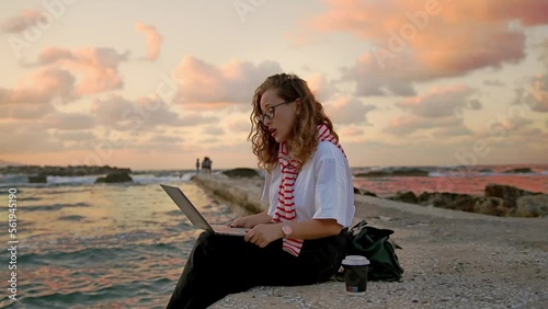 Young european women by the sea, working with a laptop on a sunset background