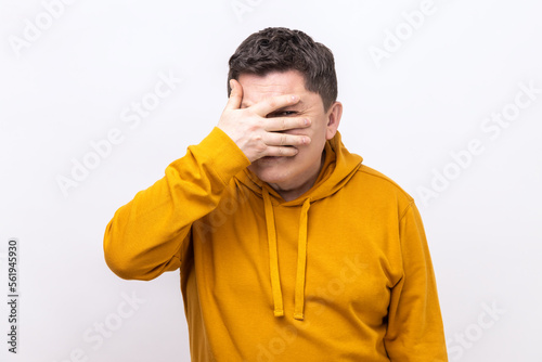 Portrait of handsome man looking through fingers, peeking with curious face, having suspicious, watching secrets, wearing urban style hoodie. Indoor studio shot isolated on white background.