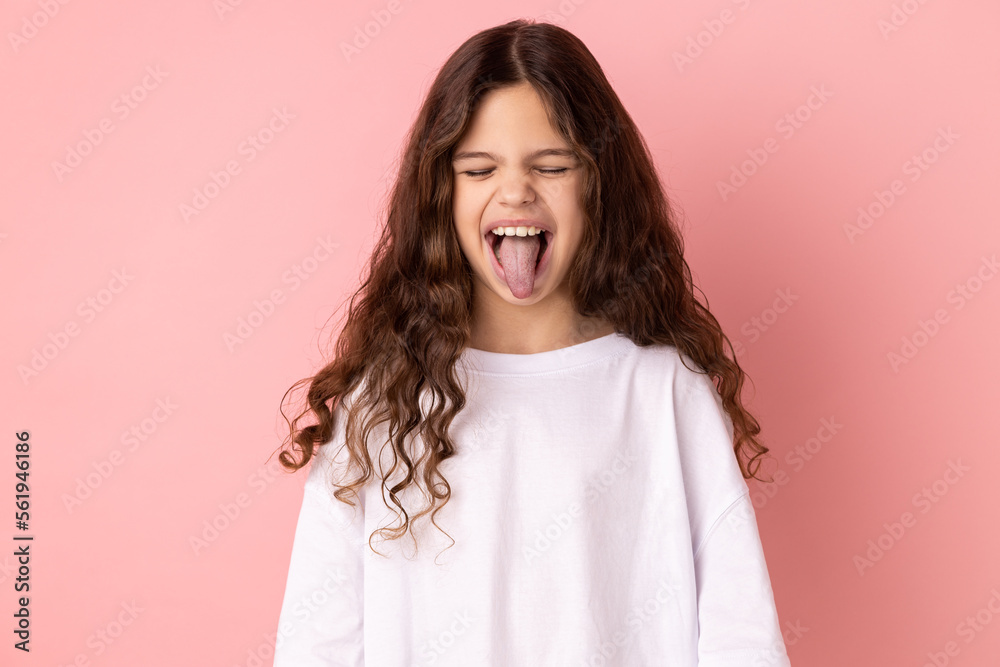 Φωτογραφία Portrait of childish carefree little girl wearing white T-shirt showing out tongue and closing eyes with naughty disobedient grimace, making face