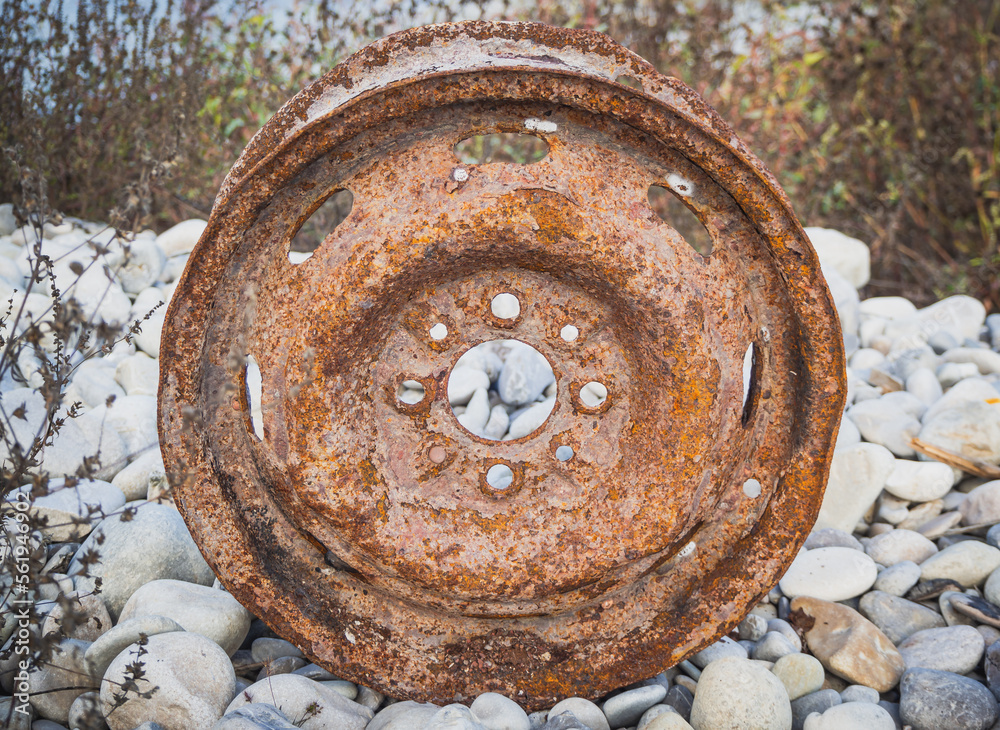 Old car wheel, rusty car alloy rim on stones by the river
