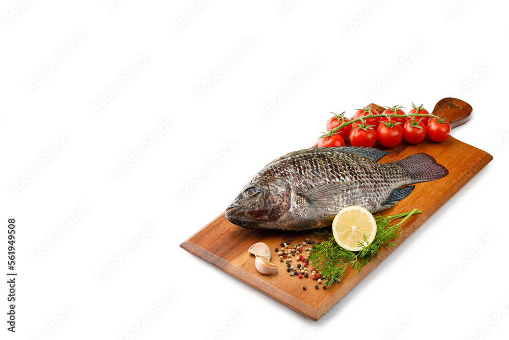 Raw fish Tilapia with spices and herbs ingredients for cooking, lemon and tomatoes on wooden cutting board isolated on white background with copy space Raw fish Tilapia with spices and herbs ingredients for cooking, lemon and tomatoes on wooden cutting board isolated on white background with copy space