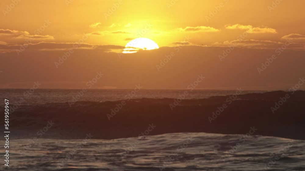 Bright sun goes down behind a cloud during orange sunset above the sea Bright sun goes down behind a cloud during orange sunset above the sea