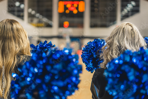 Back shot of the heads of two cheerleaders hodling blue pom-poms. Blurred background. High quality photo photo
