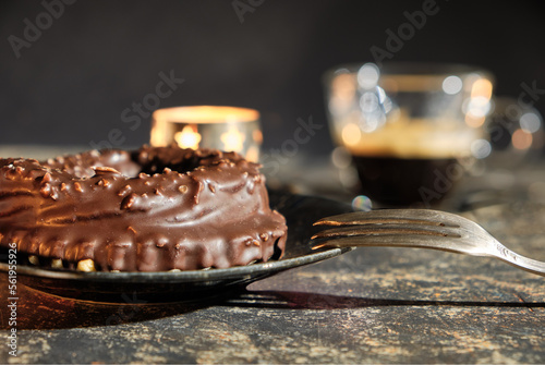 a chocolat nougat ring on a plate with a pastry fork, A glassy espresso cup and a candle light is in the bookeh