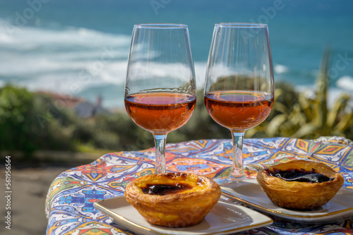 Portugal's traditional food and drink, glasses of porto wine or muscatel de setubal and dessert Pastel de nata egg custard tart pastry served with view on blue Atlantic ocean in Lisbon area, Portugal photo