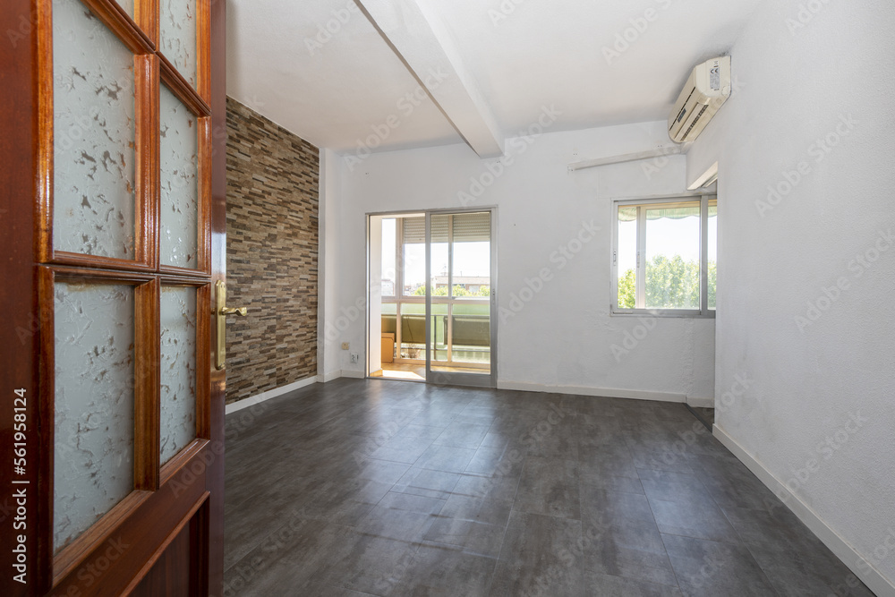 Obraz premium Empty living room with gray sintasol floors, sapele wooden door with glass and glazed terrace in the background