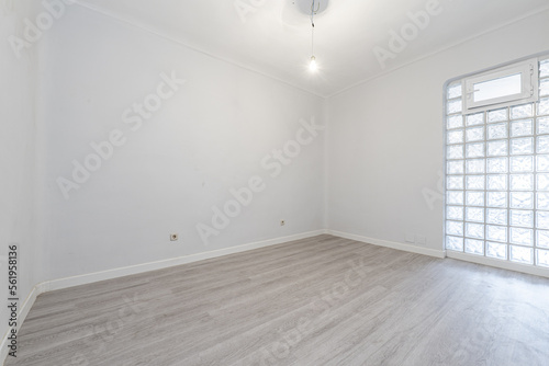 Empty room with skylight wall made of square glass pavers and light wooden floor