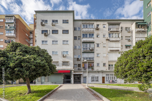 Facades of residential buildings of modest construction in a street with wide sidewalks, gardens with lawns and trees