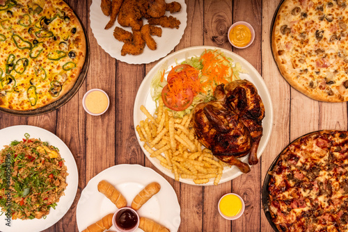 Set of varied fast food dishes, various pizzas, carbon-roasted chicken with fries and salad, fried rice, teques and fried chicken fingers photo