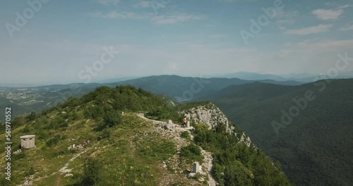 Drone shot of the top of mountain Sabotin where a hiker with an orange backpack stoped by a concrete monument. Great view of nearby mountains, Slovenian side and Italian side. photo