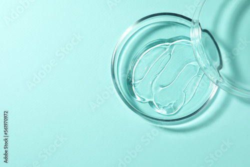 Petri dish with liquid and lid on turquoise background, top view. Space for text