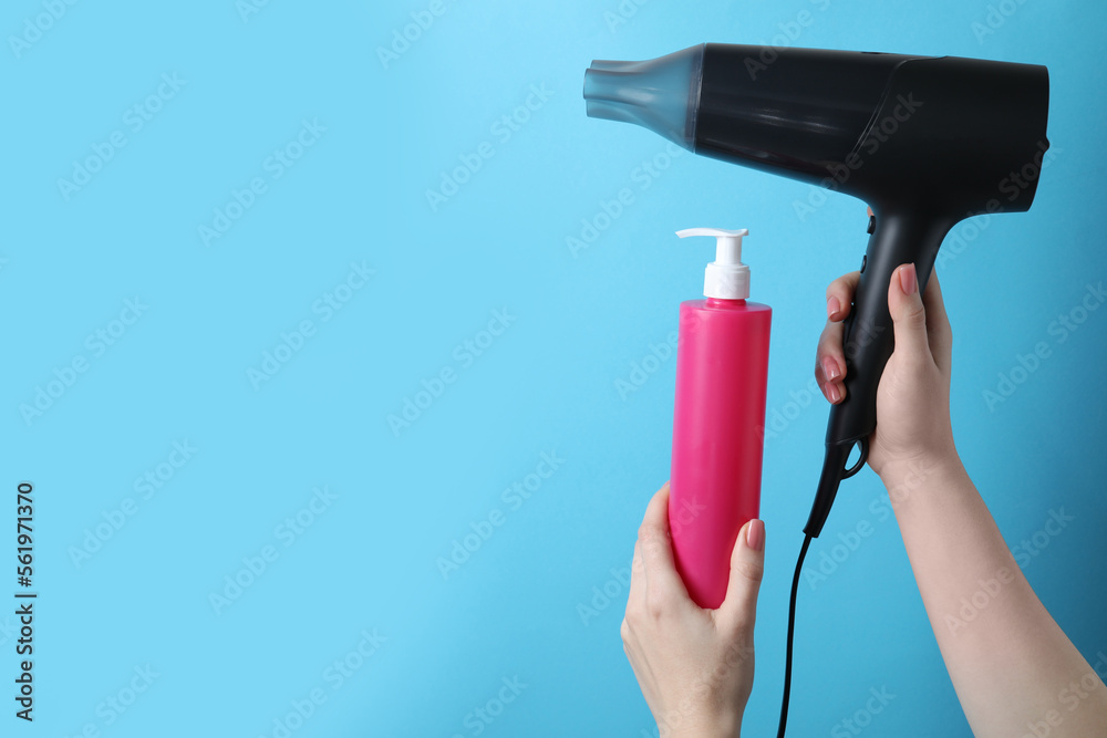 Fototapeta premium Woman holding spray bottle with thermal protection and hairdryer on light blue background, closeup. Space for text