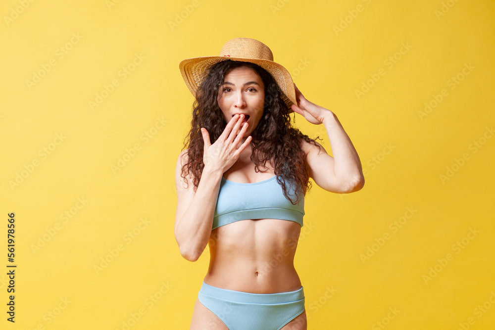 young shocked brunette girl in a blue swimsuit and with curly hair holds sunglasses on a yellow background young shocked brunette girl in a blue swimsuit and with curly hair holds sunglasses on a yellow background
