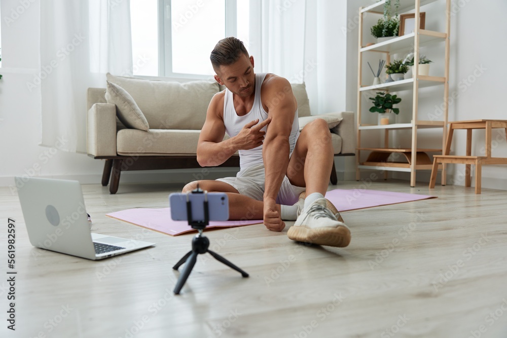 Man sports, watching tape of workout on phone and repeating exercises sports blogger with laptop training online, pumped up man fitness trainer works out at home, the concept of health and body beauty Man sports, watching tape of workout on phone and repeating exercises sports blogger with laptop training online, pumped up man fitness trainer works out at home, the concept of health and body beauty