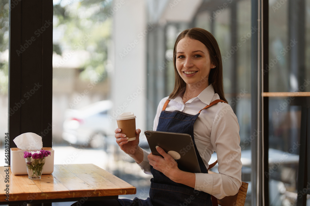 Young Female manager in restaurant with tablet. Woman coffee shop owner with open sign. Small business concept Young Female manager in restaurant with tablet. Woman coffee shop owner with open sign. Small business concept