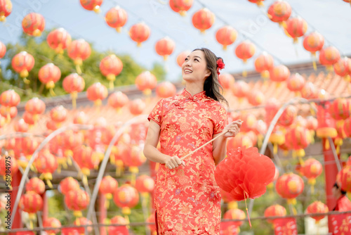Beautiful Asian woman wearing traditional cheongsam qipao dress looking confident holding lantern in Chinese Buddhist temple. Celebrate Chinese lunar new year, festive season holiday. Emotion smile