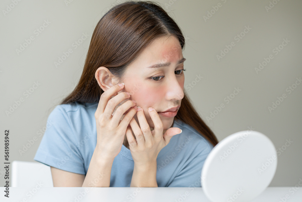 Dermatology, scratch asian young woman looking at mirror, expression worry and itch, itchy allergy or allergic sensitive reaction, red spot or rash on her face. Beauty care from skin problem treatment Dermatology, scratch asian young woman looking at mirror, expression worry and itch, itchy allergy or allergic sensitive reaction, red spot or rash on her face. Beauty care from skin problem treatment