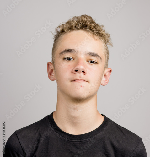 Portrait of a young boy or teenager with a funny facial expression and pimples behind a neutral background.