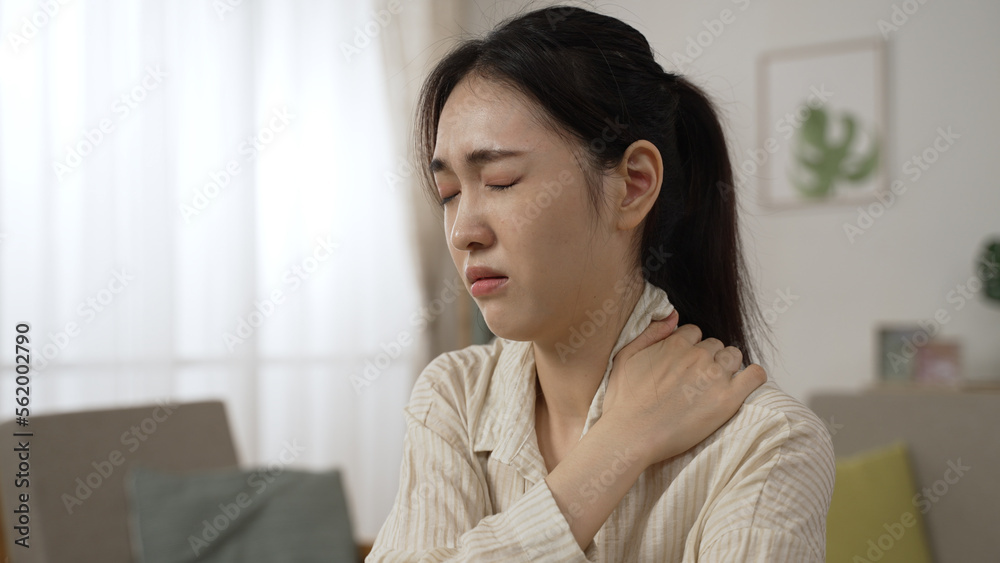 asian female freelance worker having a sudden neck crick is massaging her stiff shoulders and relaxing her muscles while working at home in the living room asian female freelance worker having a sudden neck crick is massaging her stiff shoulders and relaxing her muscles while working at home in the living room