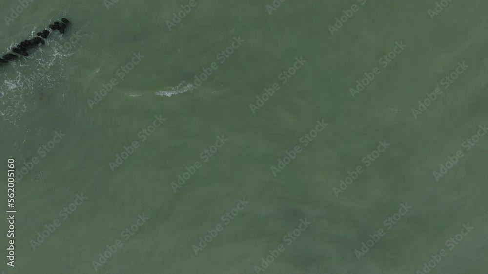 Aerial birdseye view of an old wooden pier at the Baltic sea coastline, overcast winter day, white sand beach, wooden poles, waves hitting shore, wide drone dolly shot moving left Aerial birdseye view of an old wooden pier at the Baltic sea coastline, overcast winter day, white sand beach, wooden poles, waves hitting shore, wide drone dolly shot moving left