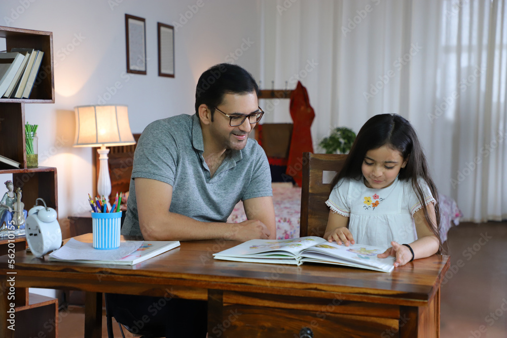 Portrait of smiling father helping cute daughter reading a storybook - Childhood Parenting Concept. Royalty free image of a happy father sitting with a little beautiful daughter on chair - helping... Portrait of smiling father helping cute daughter reading a storybook - Childhood Parenting Concept. Royalty free image of a happy father sitting with a little beautiful daughter on chair - helping...