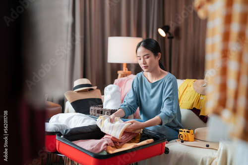 asian young mature adult female woman ready to travel, asian female wear casual cloth arrange packing cloth in suitcase luggage and stuff on the floor in living room for travel after lockdown is over