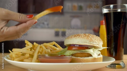 A female eating french fries with tomato ketchup - appetizer  deep fried  high cholesterol diet  sugary cola. A tasty delicious burger is served with cold drinks and potato fries - fast food  popul... photo